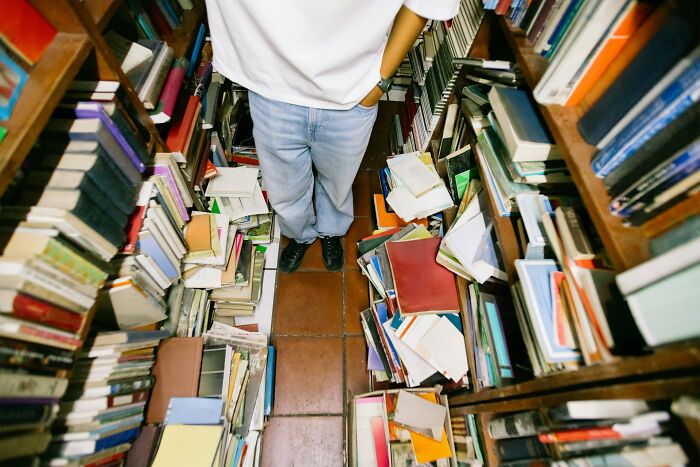Person standing among cluttered bookshelves filled with disorganized books illustrating snobbish behavior in a busy setting