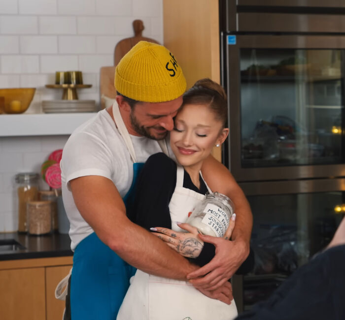 Ariana Grande with a man in a kitchen, sharing a warm embrace amid discussions of her struggles and family support.