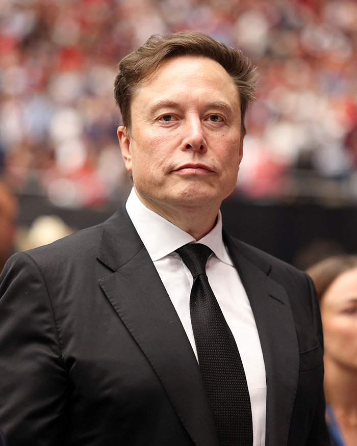 Elon Musk in a black suit and tie at a public event, linked to his comment sparking an online frenzy about Sydney Sweeney.