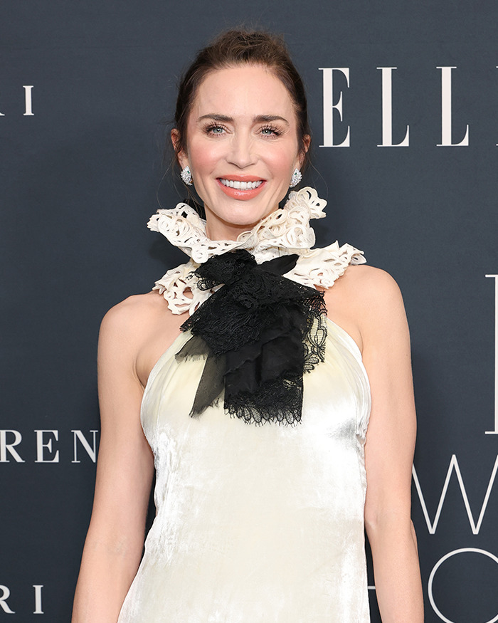 Emily Blunt smiling in a cream dress with lace details, fueling plastic surgery rumors after podcast appearance.