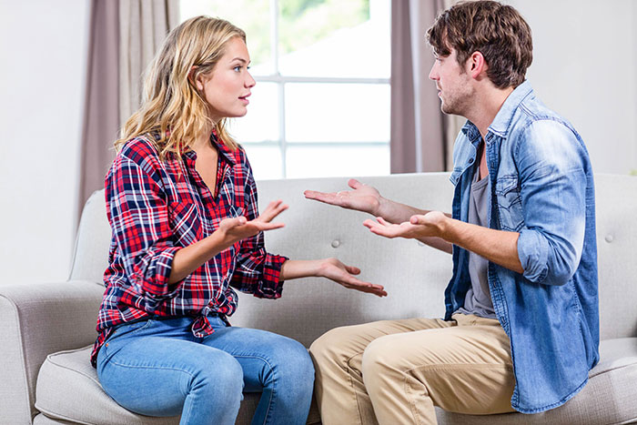 Young couple arguing on a couch about entitled mother expenses split with son's girlfriend in a bright living room.