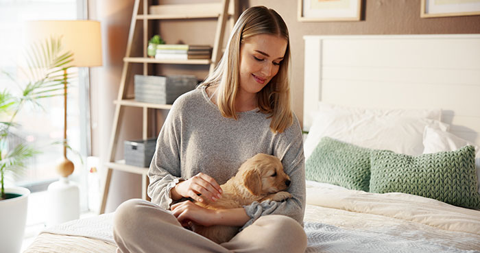 Young woman sitting on bed, smiling while holding a puppy, highlighting entitled mother expenses and split family themes.