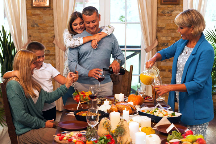 Family enjoying Thanksgiving dinner together with food and drinks on the table in a warm, cozy dining room setting. Family enjoying Thanksgiving dinner together with food and drinks on the table in a warm, cozy dining room setting.