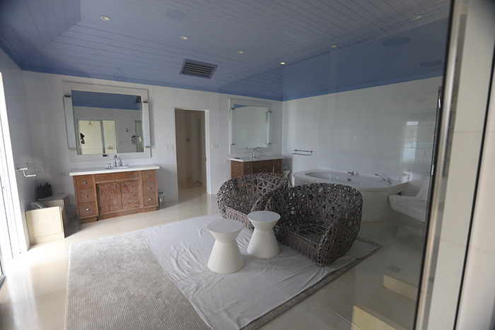 Spacious bathroom inside Epstein&rsquo;s private island home featuring wicker chairs, twin sinks, and a large bathtub.
