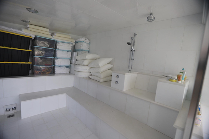 Sterile tiled bathroom inside Epstein&rsquo;s private island home with shower and stacked pillows and storage containers.