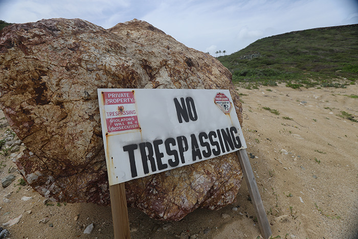 No trespassing sign on sandy ground near large rock at Epstein&rsquo;s private island home, eerie restricted area view.