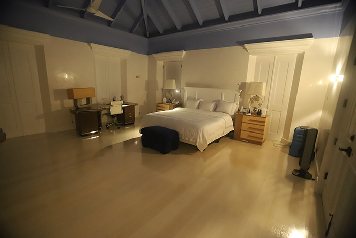 Spacious bedroom inside Epstein&rsquo;s private island home with a large bed, desk, and soft, dim lighting at night.