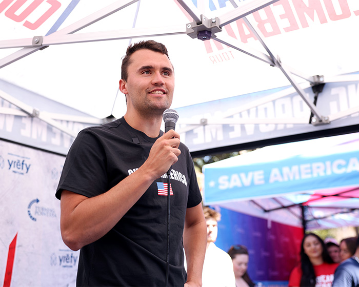 Man holding microphone at an outdoor event, associated with Erika Kirk accused of cashing in promoting Charlie Kirk&rsquo;s book.