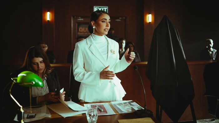 A woman in a white suit passionately presenting a case in a courtroom, highlighting moral compass dilemmas and decisions.