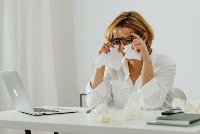 Woman wiping tears with tissues at desk near laptop, facing emotional moral compass dilemmas and decision-making challenges.