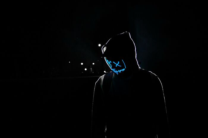 Person wearing a hood and glowing mask in darkness symbolizing moral compass challenged by shocking dilemmas at night