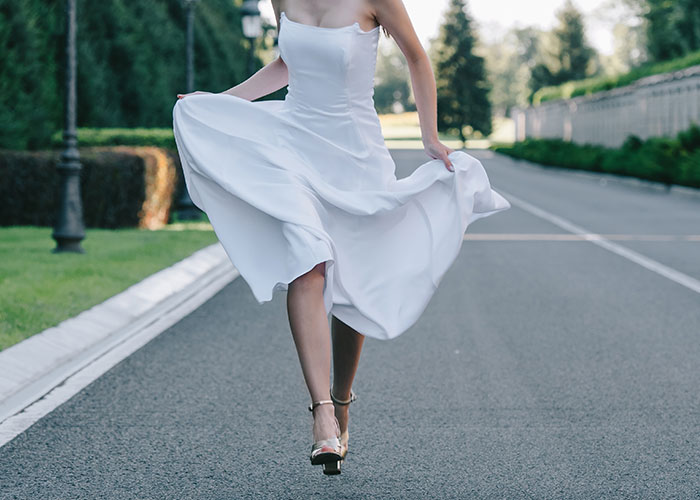 Bride in white dress running away on empty road symbolizing fiancé disappears before wedding and man left without closure.