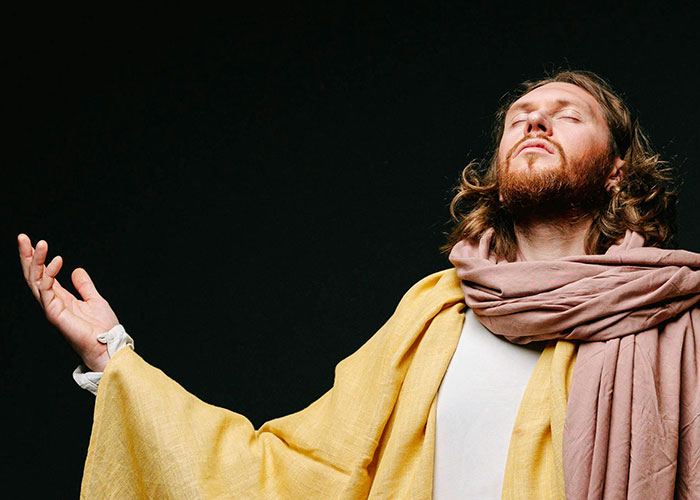 Man in yellow robe and scarf with eyes closed and arms raised, capturing the moment of realizing a cult experience.
