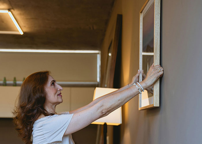 Middle-aged woman hanging a picture frame on the wall, symbolizing people sharing the moment they realized they are in a cult.