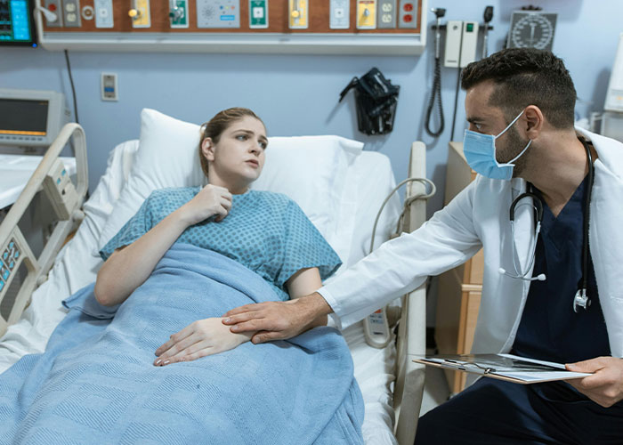 Patient in hospital bed looking concerned as doctor wearing mask comforts her, illustrating people sharing cult realization moments.