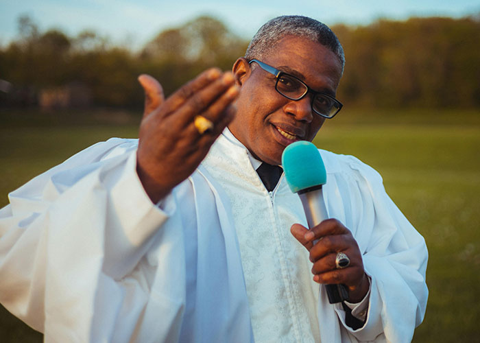 Man in religious robe holding microphone outdoors, symbolizing people sharing the moment they realized they are in a cult
