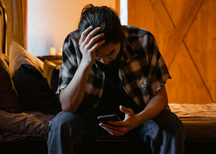Man sitting on bed holding phone with hand on head, reflecting on the moment they realized they are in a cult.