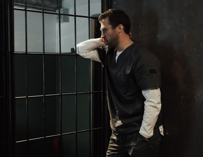 Man in dark clothing looking distressed inside a room with bars, reflecting family stalks and disownment issues.