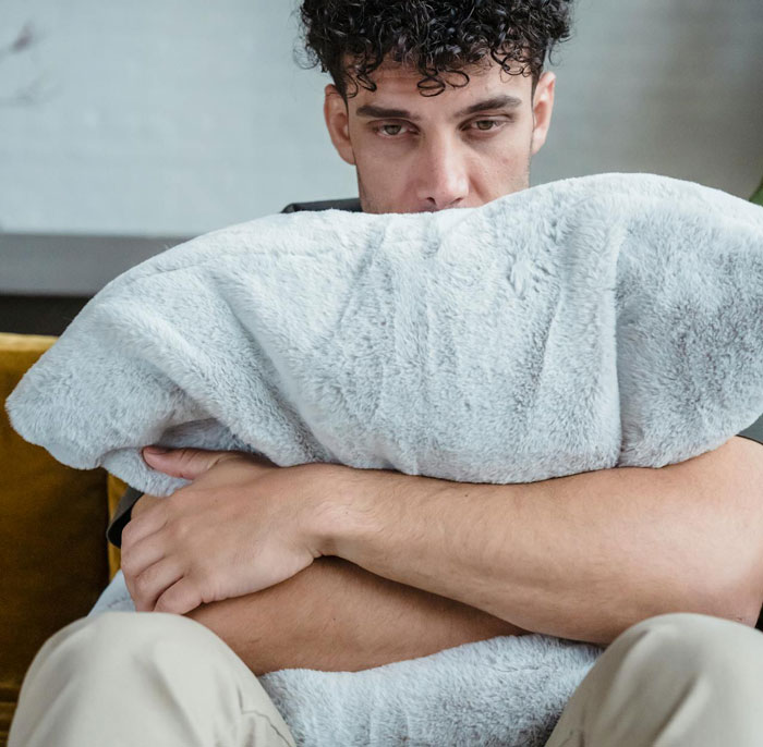 Young man hugging a pillow, looking sad and troubled, depicting emotions of shame guilt and family disownment.