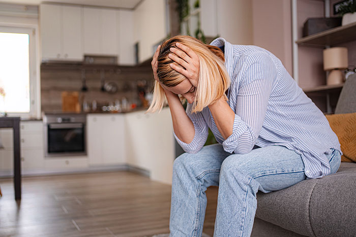 Woman feeling distressed and regretful after Thanksgiving dinner, sitting on a couch with head in hands in a kitchen. Woman feeling distressed and regretful after Thanksgiving dinner, sitting on a couch with head in hands in a kitchen.