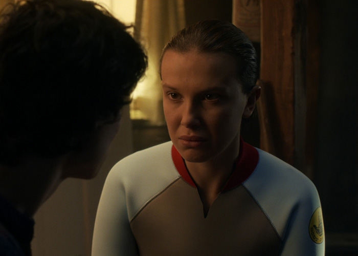 Millie Bobby Brown in a tense scene from Stranger Things, with dramatic lighting highlighting her focused expression.