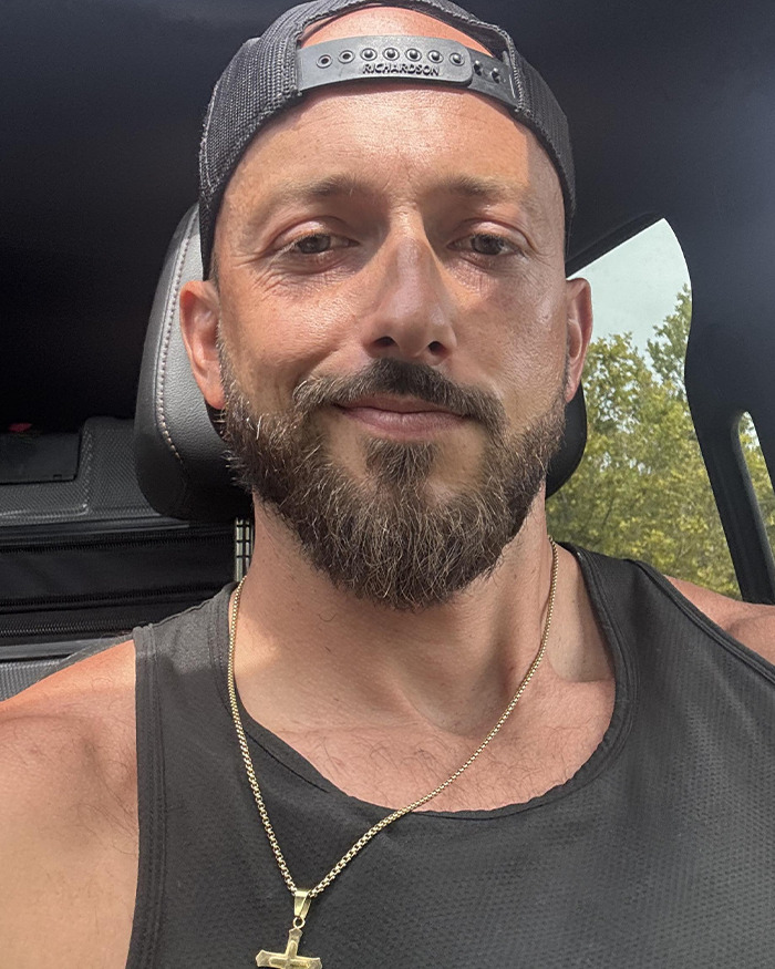 Man wearing a backward cap and gold cross necklace inside a car, conveying emotions related to children's heartbreaking words.