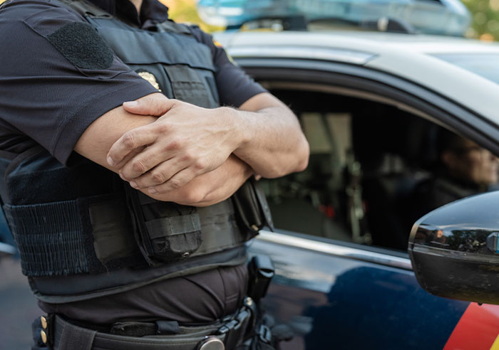 Police officer standing with arms crossed near patrol car illustrating restraining order enforcement against MIL after marriage conflict.