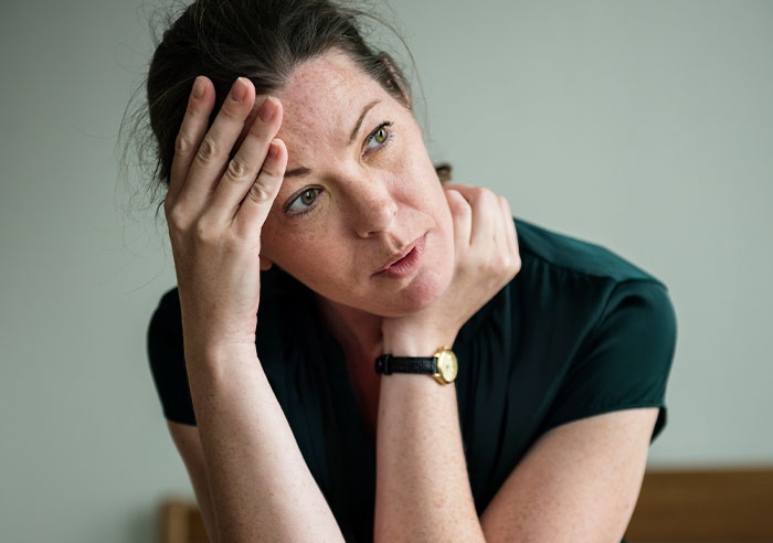 Woman looking distressed and thoughtful indoors, illustrating a restraining order situation involving a mother-in-law conflict.