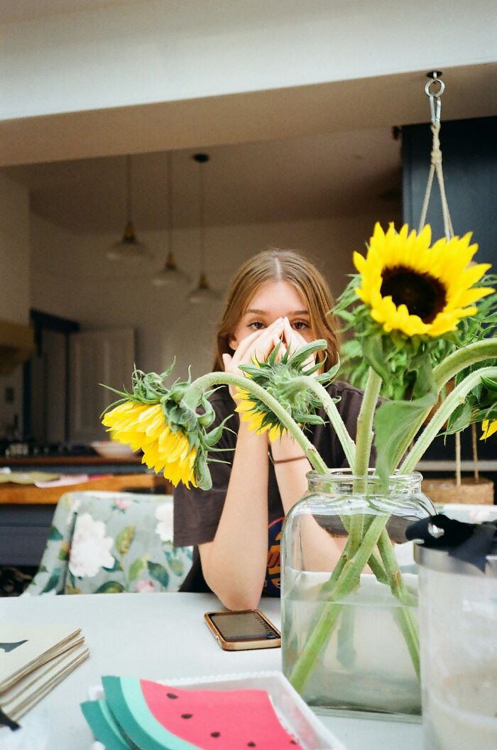 Young woman sitting at a table with sunflowers in a vase, appearing thoughtful about secretly seeing a guy with a girlfriend. Young woman sitting at a table with sunflowers in a vase, appearing thoughtful about secretly seeing a guy with a girlfriend.