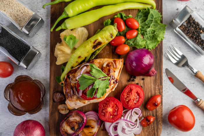 A wooden board with grilled chicken, fresh tomatoes, onions, peppers, and other veggies promoting teen health meals. A wooden board with grilled chicken, fresh tomatoes, onions, peppers, and other veggies promoting teen health meals.