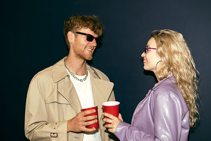 Young girl and friend laughing and roasting each other with playful insults while holding red cups at a party