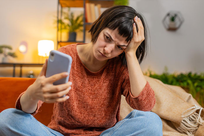 Young woman in a sweater looking frustrated while holding a phone, depicting ghosting after getting a boyfriend.