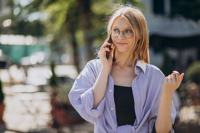 Young woman with glasses talking on phone outdoors, symbolizing a bestie ghosting writer seeking help to break into Hollywood.