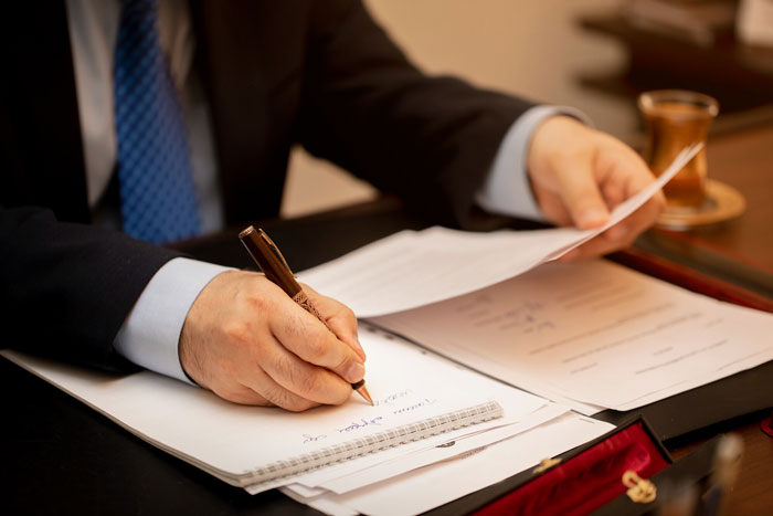 Man in suit writing notes on paper while holding documents, illustrating communication about funeral wishes and hometown reaction.