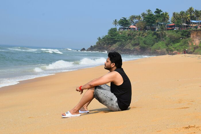 Man sitting on a sandy beach looking at the ocean, illustrating patients coming off anesthesia being funny and relaxed.