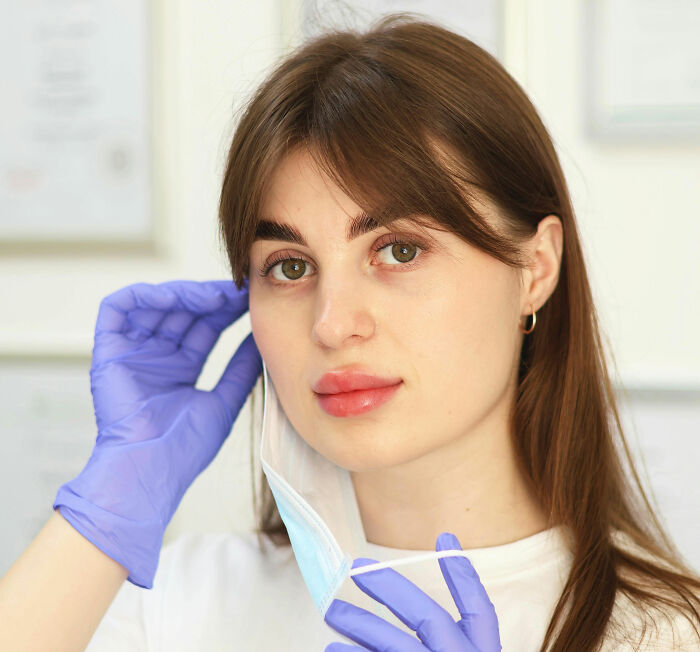 Medical staff wearing purple gloves removing face mask in clinical setting with light background and certificates.