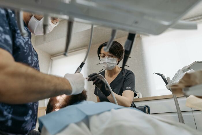 Medical staff in masks and gloves attending to a patient in a clinical setting during anesthesia recovery.