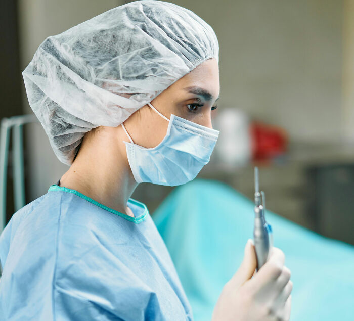 Medical staff in protective gear focusing on a dental tool while preparing patients coming off anesthesia in clinic.