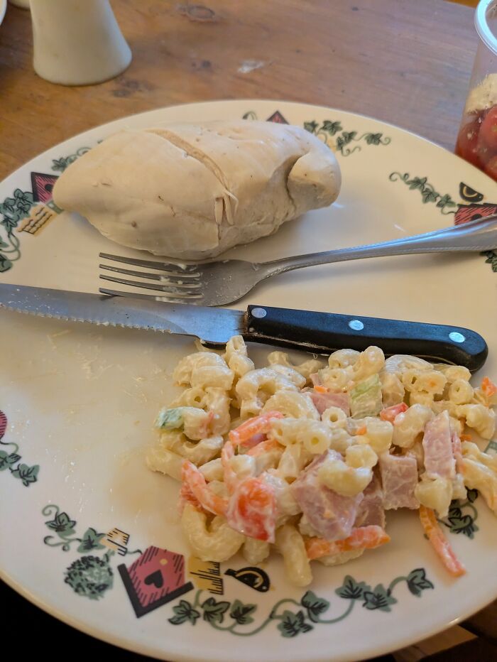 Unappetizing food pic featuring a plain, c*****d chicken breast and a small serving of creamy macaroni salad.