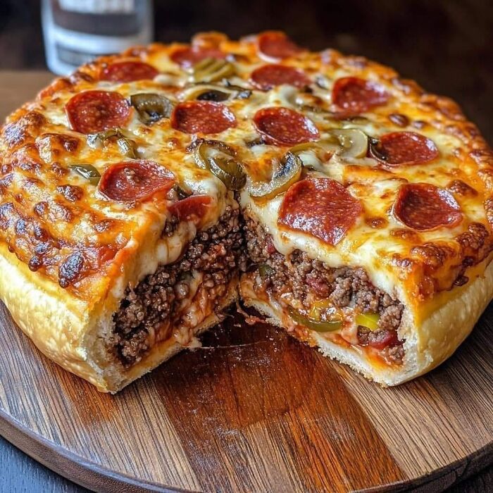 Deep dish pepperoni and mushroom pizza stuffed with ground beef, cheese, and peppers on a wooden serving board.