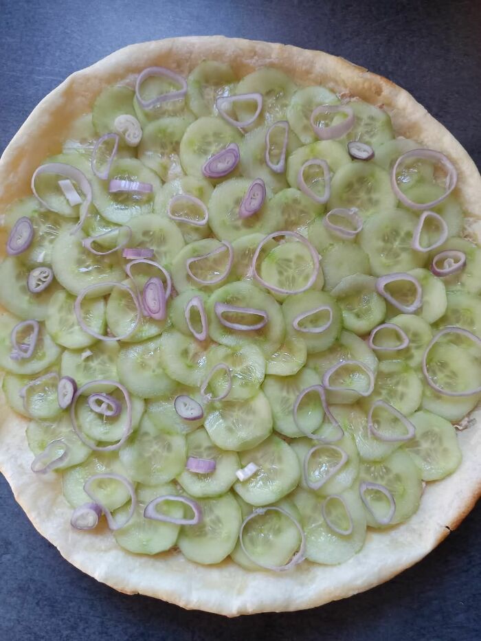 Pizza crust topped with thinly sliced cucumbers and red onion rings, a food pic that deserves to be shamed online