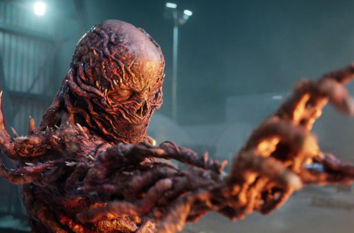 Horrific creature from Stranger Things Season 5 reaching forward in a dimly lit industrial setting.