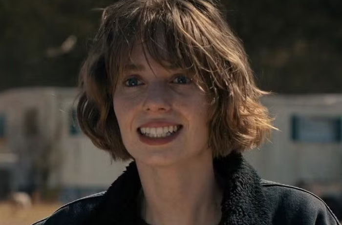 Smiling character from Stranger Things Season 5 outdoors with blurred background during a daytime scene.