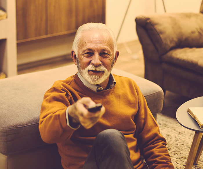 Elderly man smiling on couch pointing remote, capturing funny moments parents said watching Stranger Things season 5.