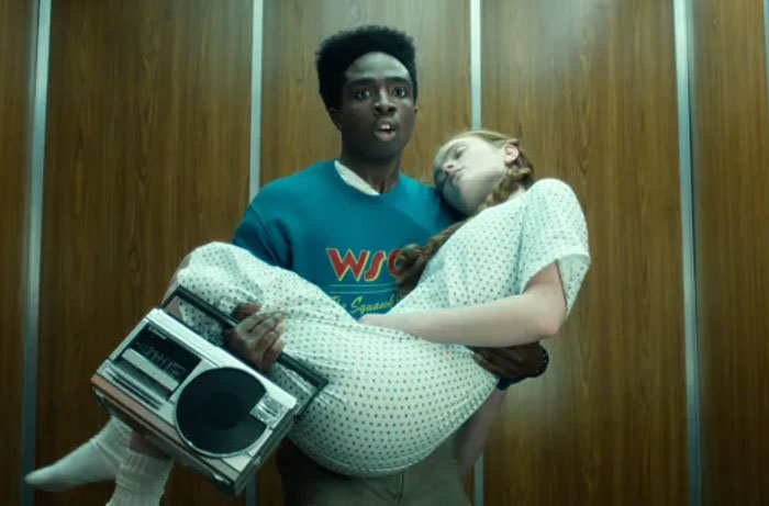 Young man carrying unconscious girl in hospital gown, a scene from Stranger Things season 5 with parents sharing funny moments