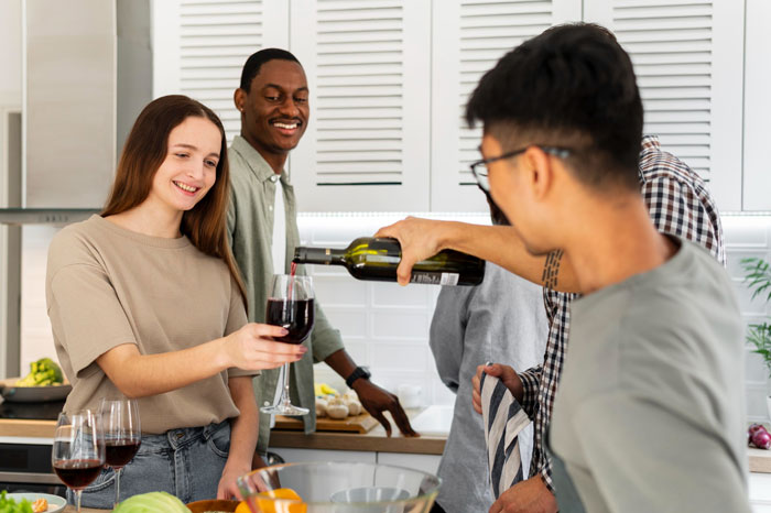 Woman happily accepting wine poured by friend during casual gathering with buddies in kitchen setting Woman happily accepting wine poured by friend during casual gathering with buddies in kitchen setting
