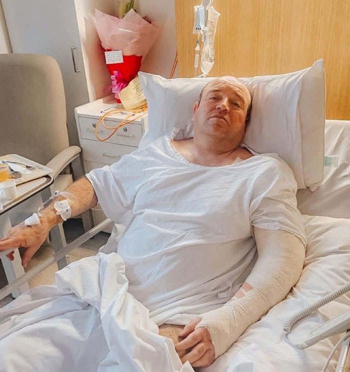 Man with bandaged arm lying in hospital bed recovering after Bondi Beach attack, relating to swimwear model controversy.