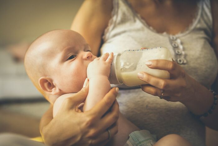 Baby drinking from a bottle held by an adult, highlighting a moment of caring interaction and snobbish behavior online.