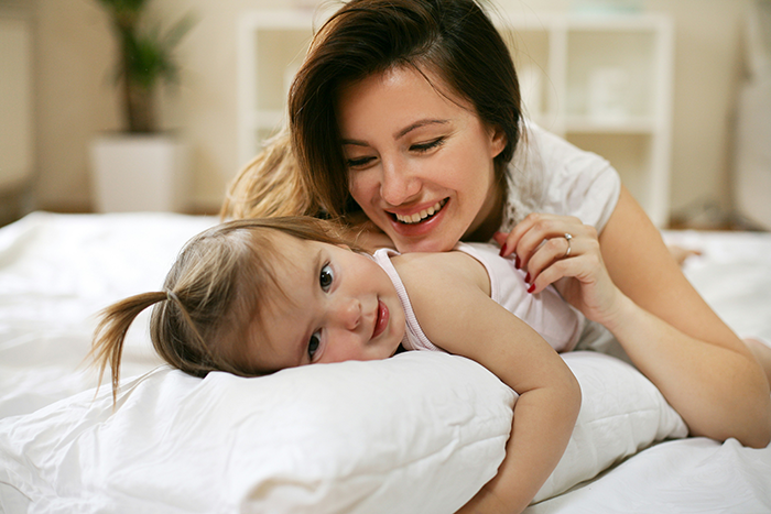 Military mother teaching toddler while lying on a bed, sharing a joyful and intimate moment at home.
