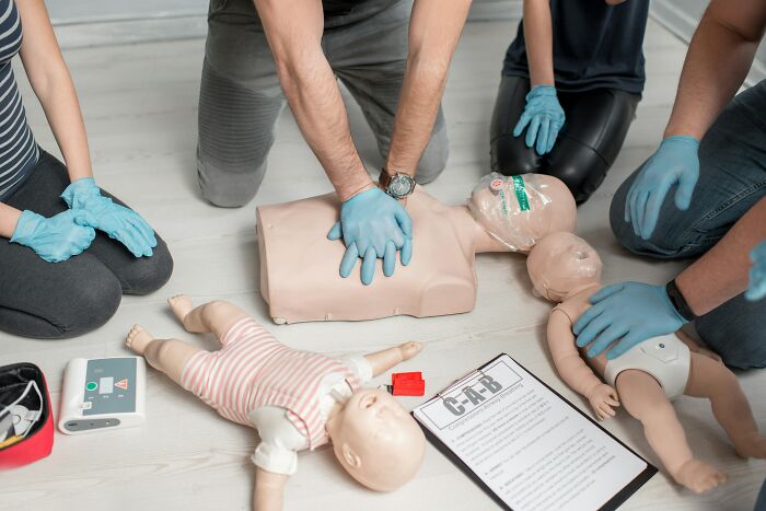 Group of people wearing gloves practicing CPR on adult and infant mannequins demonstrating disturbing science facts.